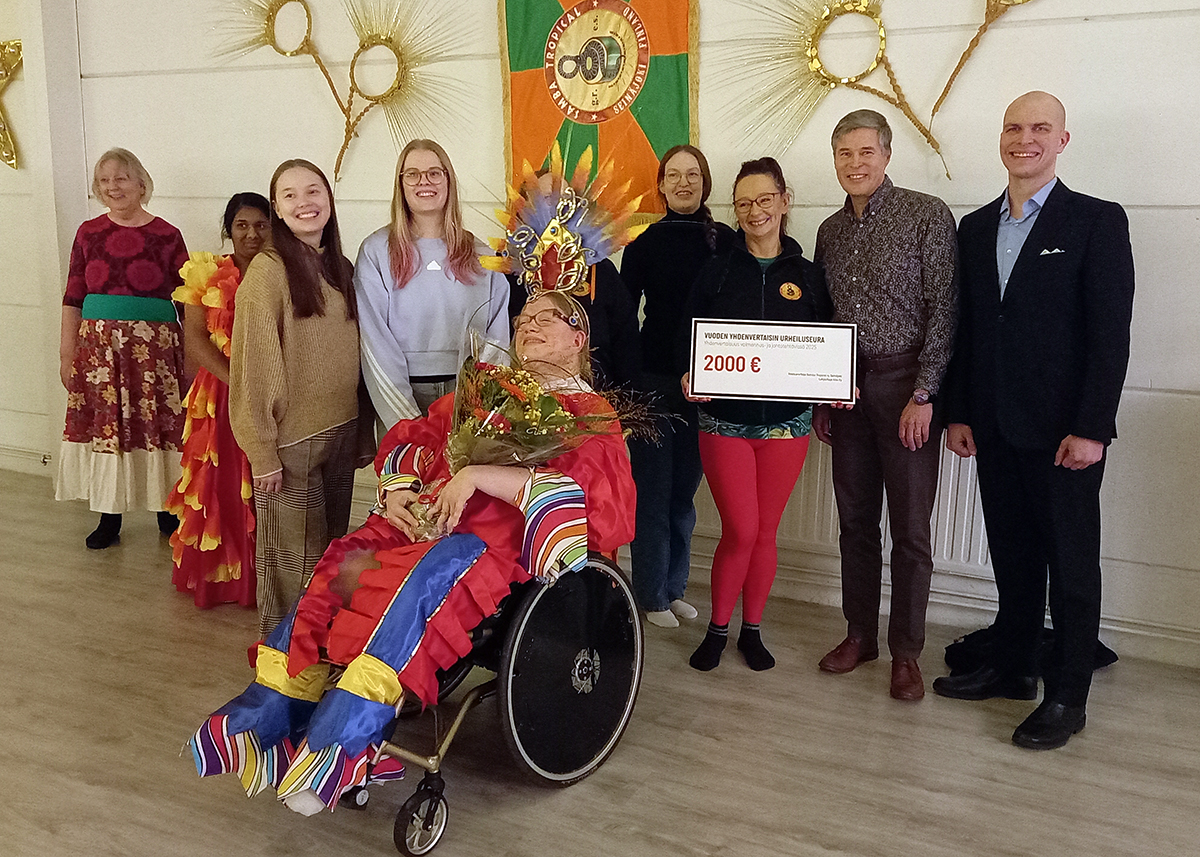 Samba Tropicalin tanssijoita ja taustahenkilöitä yhteiskuvassa Alkon ja Paralympiakomitean edustajien kanssa joulukoristeiden keskellä.